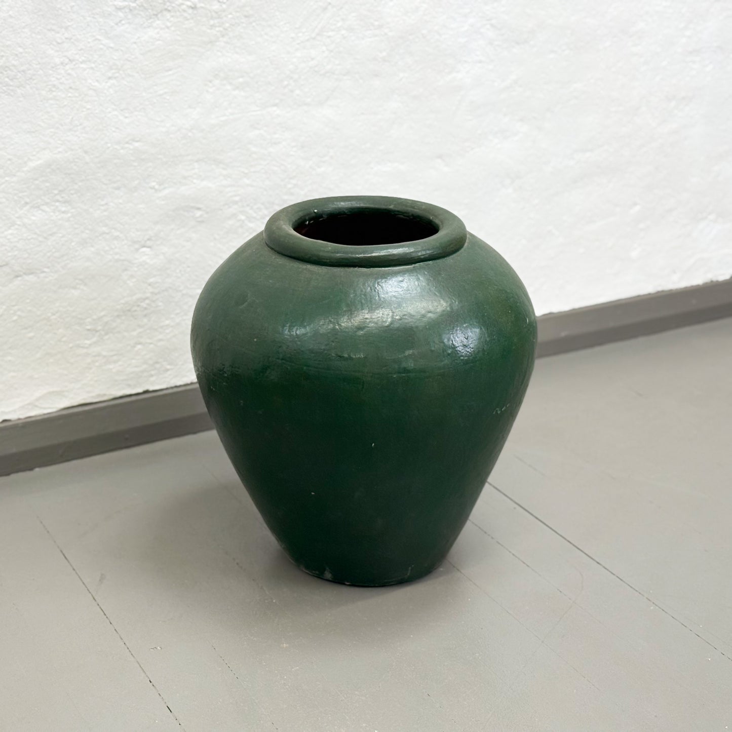 Green ceramic jar on a white floor with a white textured wall background