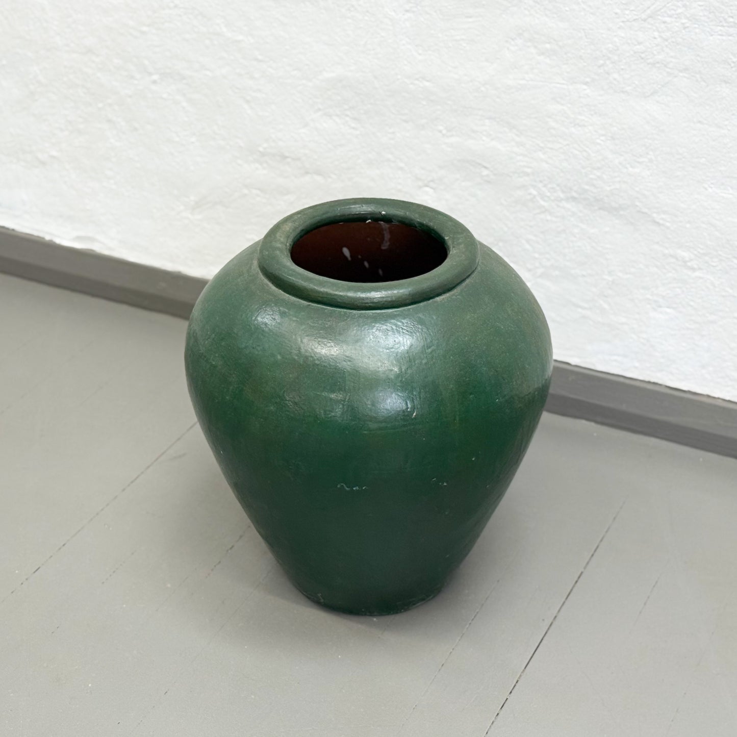 Green ceramic jar on a white floor with a textured white wall background