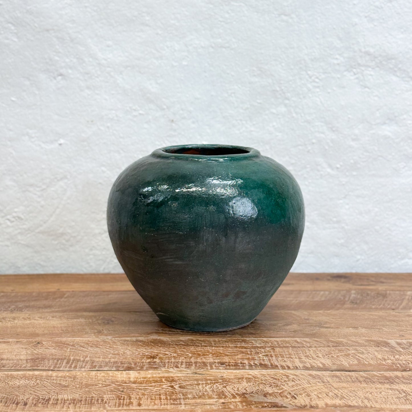 Green ceramic vase on a wooden surface with a textured white wall background