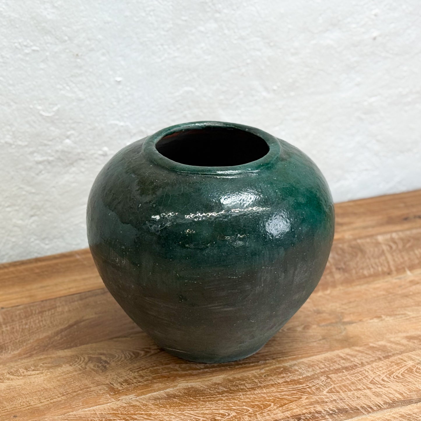 Green ceramic vase on a wooden surface with a white textured wall background