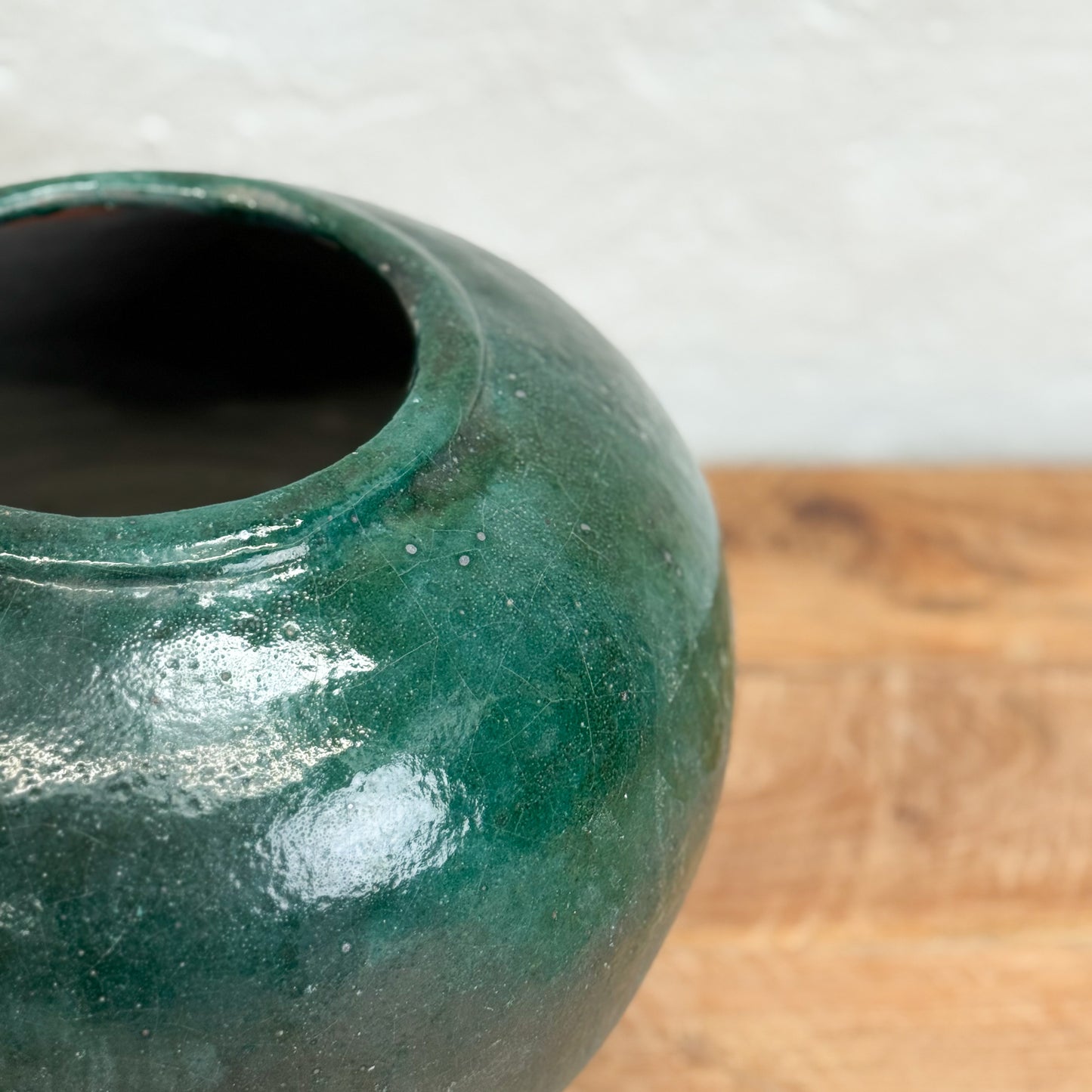 Green ceramic pot on a wooden surface with a blurred background