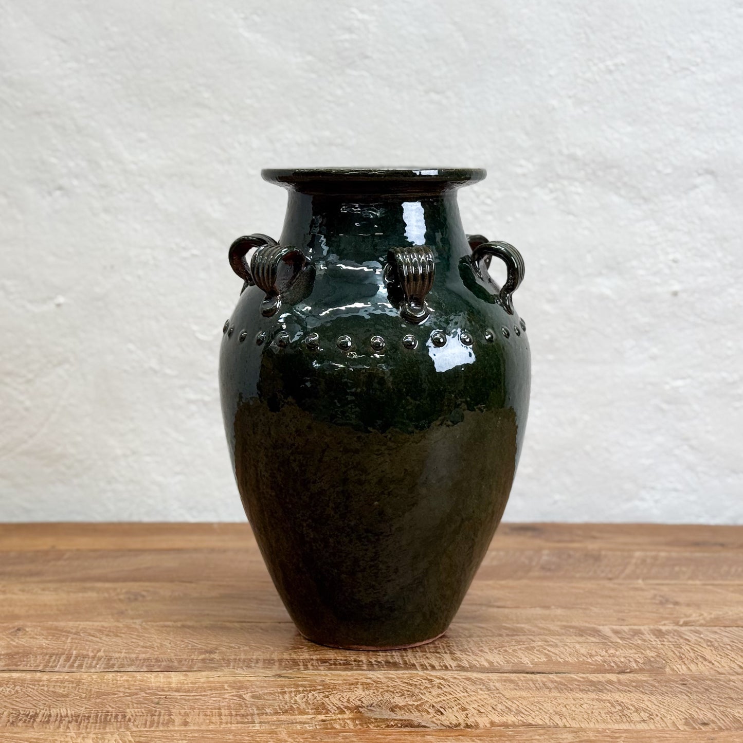 Black ceramic vase with handles on a wooden surface and white textured wall background