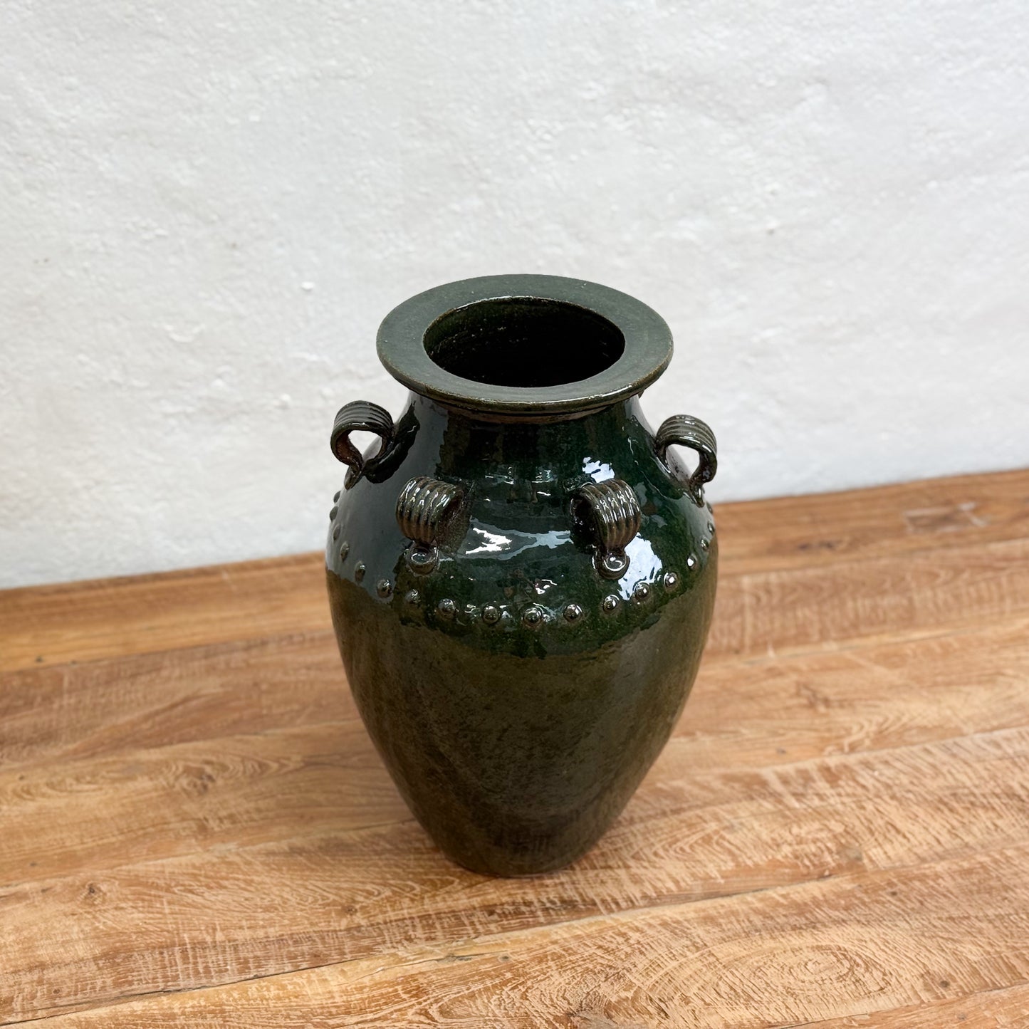 Green ceramic vase with decorative handles on a wooden surface