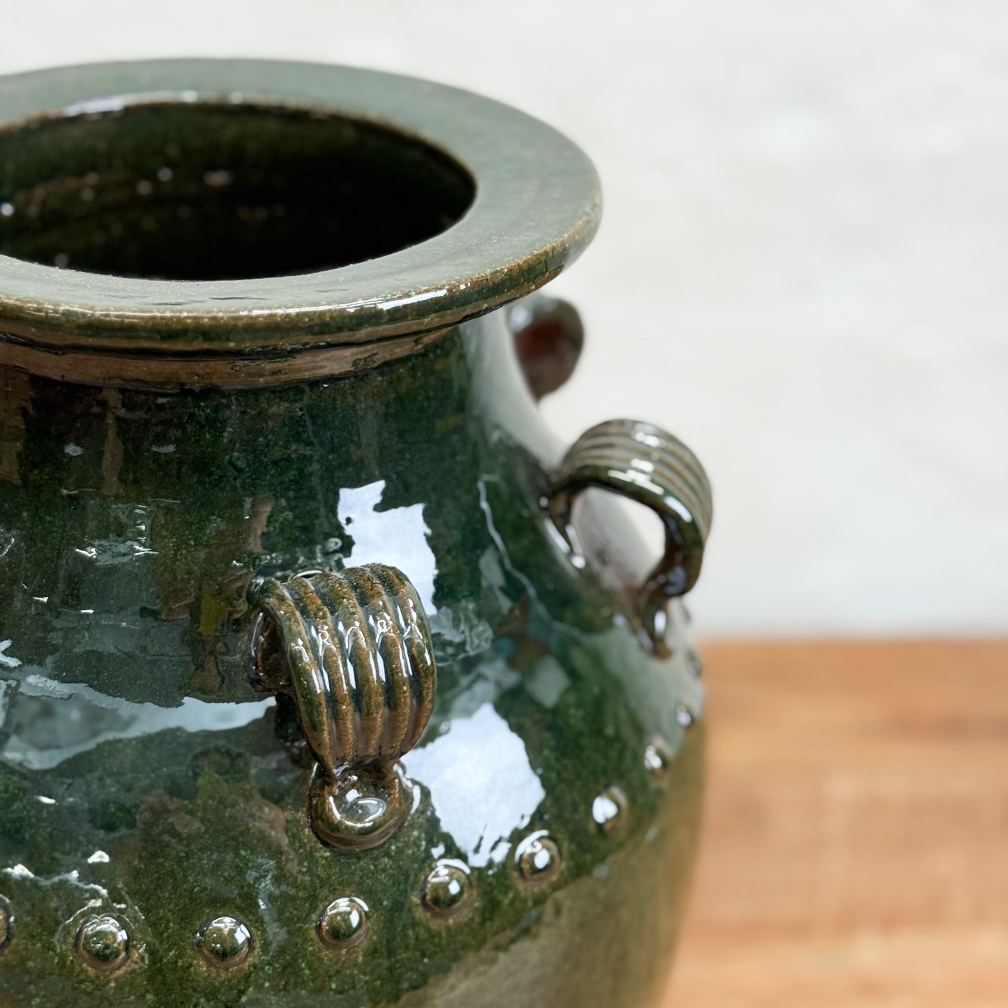 Green ceramic vase with decorative handles on a wooden surface