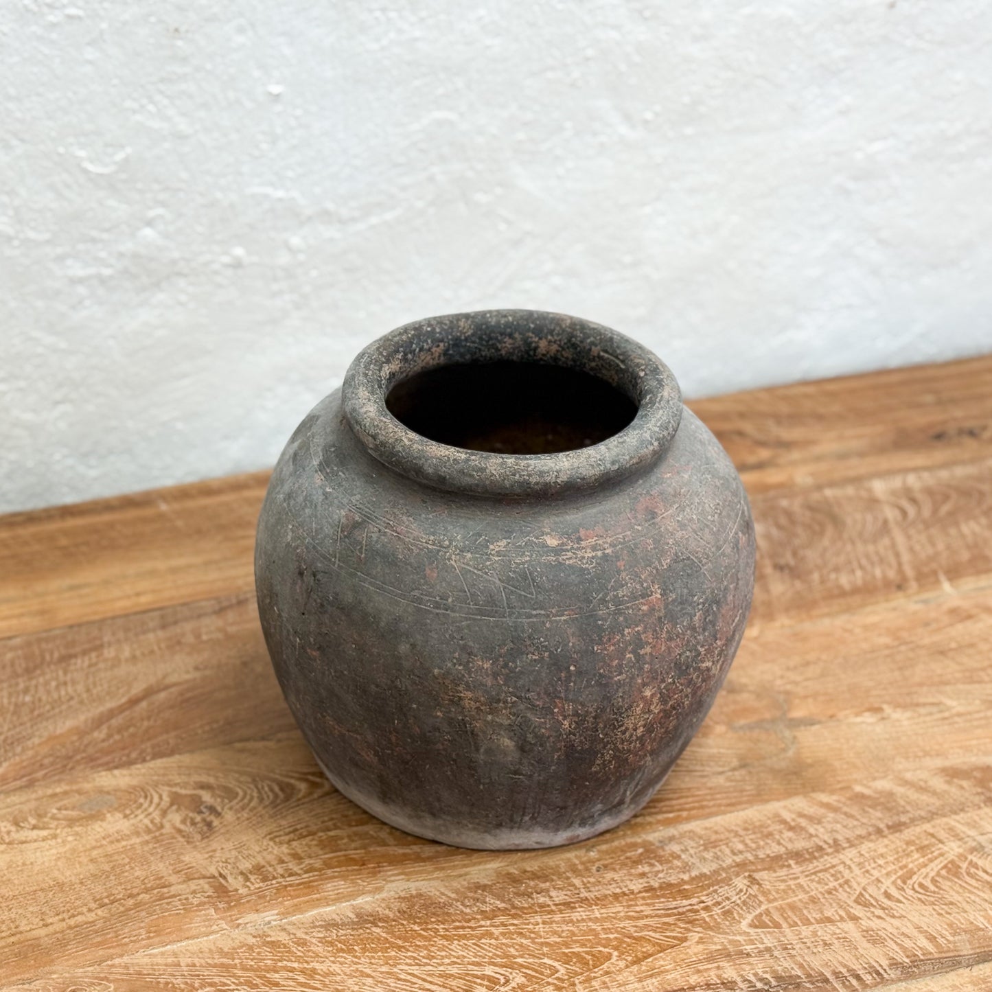 Vintage terracotta pot on a wooden surface with a white textured wall background
