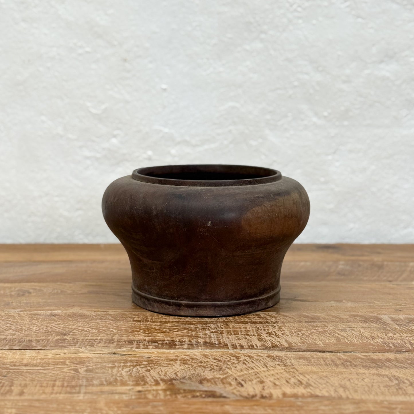 Brown ceramic pot on a wooden surface with a textured white wall background