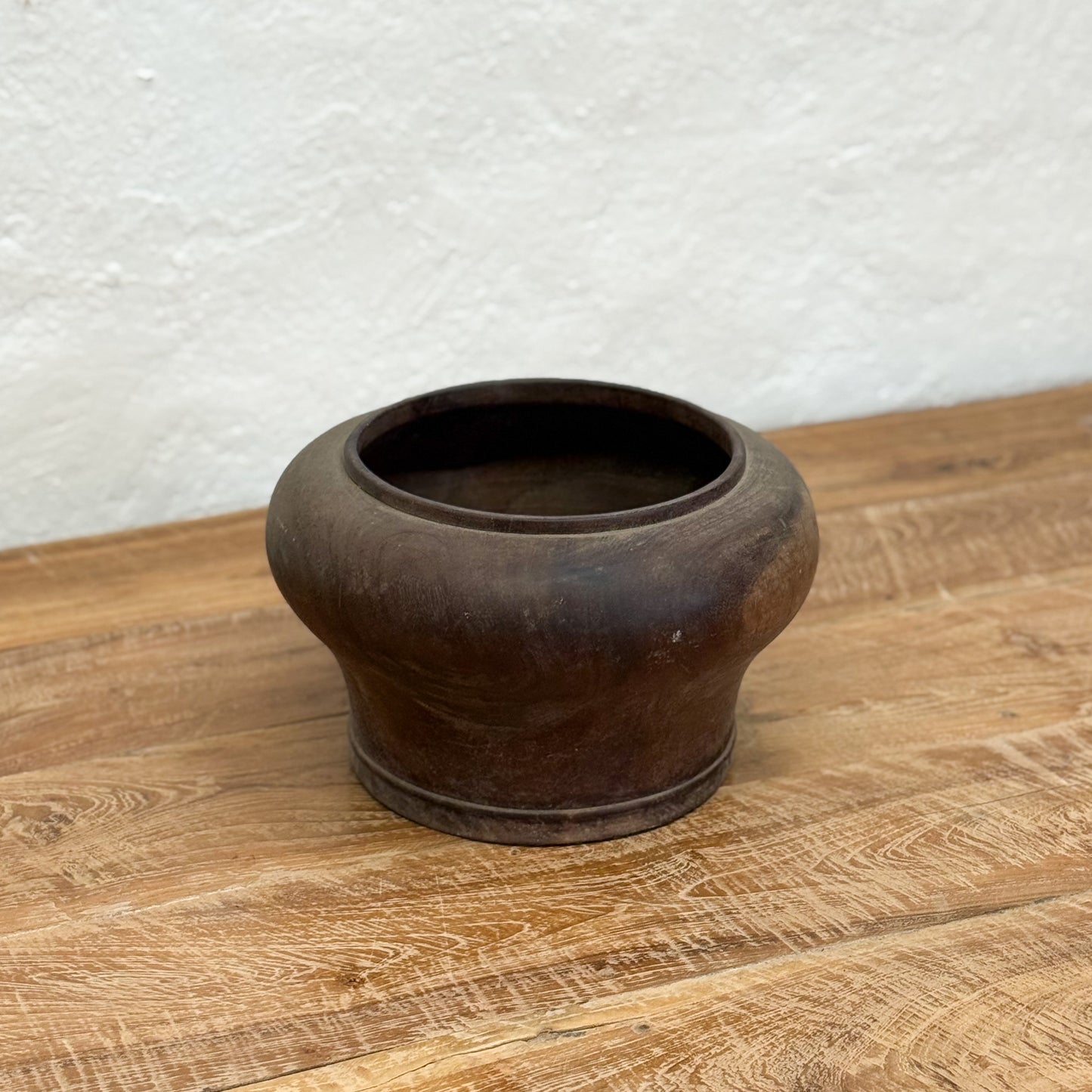Dark brown ceramic pot on a wooden surface with a light gray textured background