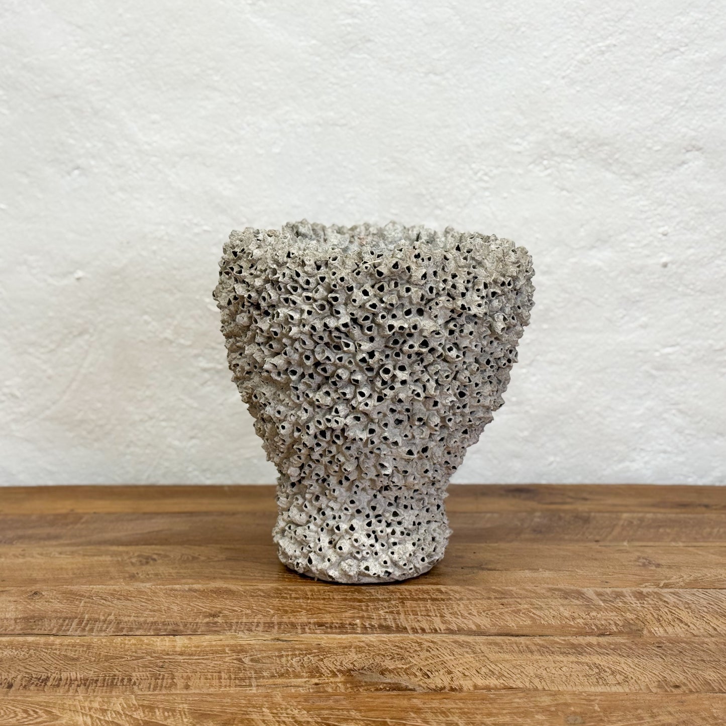 Textured ceramic vase on a wooden surface with a white textured wall background