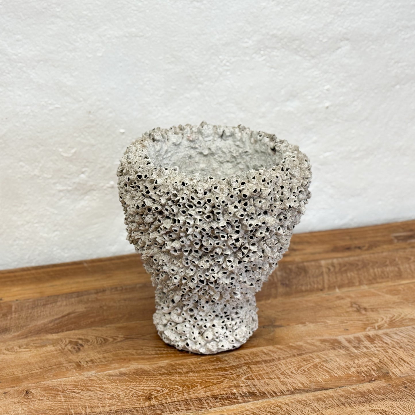 Textured vase on a wooden surface with a white textured wall background