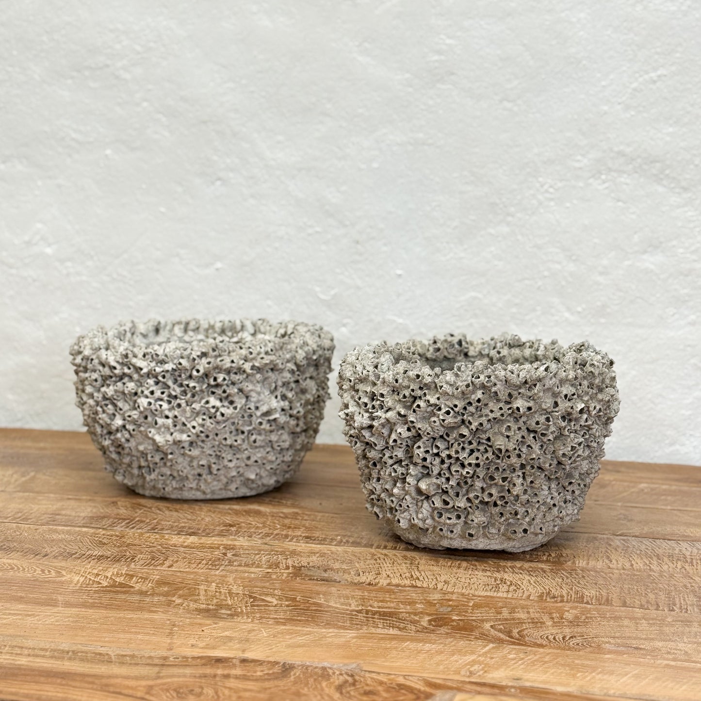 Two textured stone bowls on a wooden surface with a light gray background