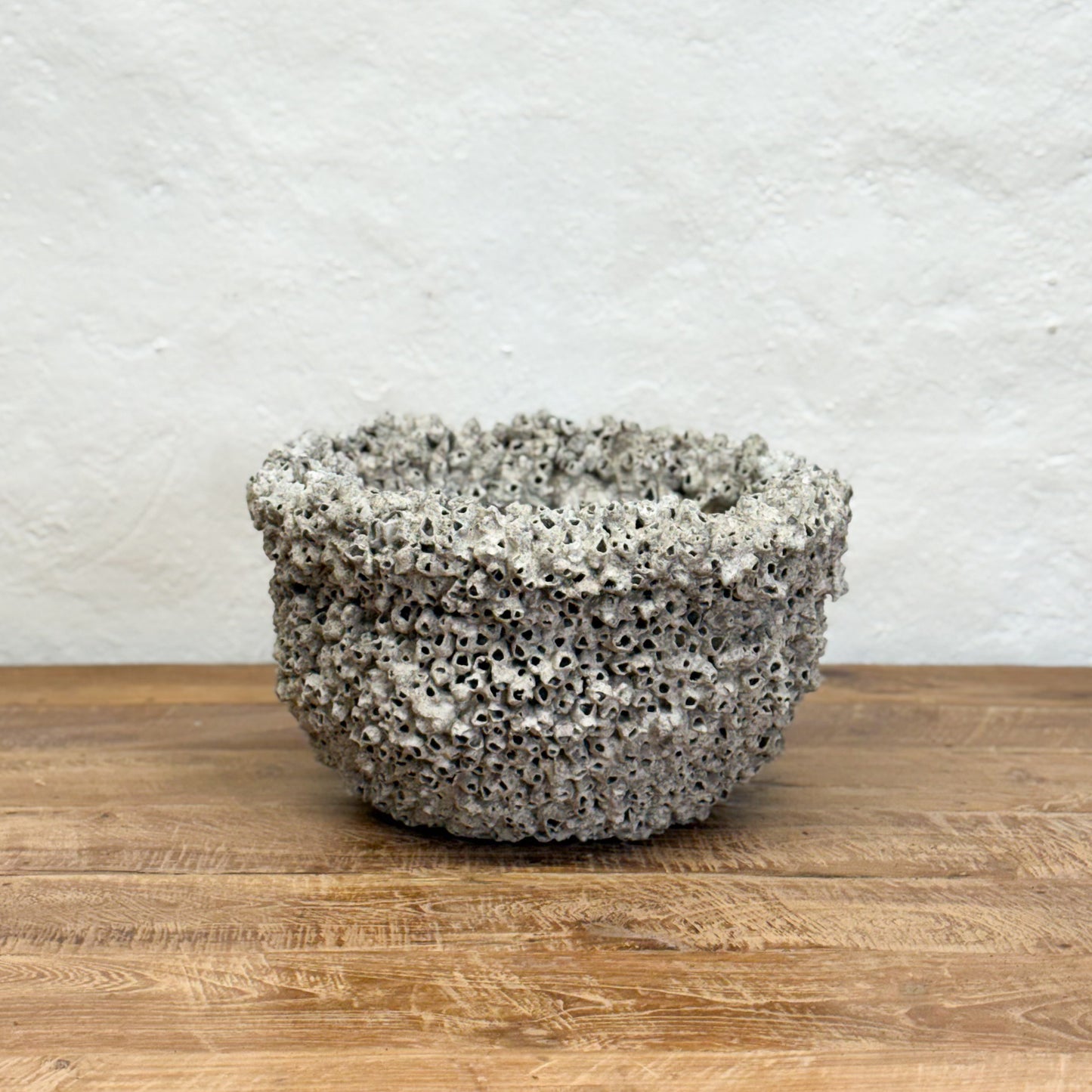 Textured ceramic bowl on a wooden surface with a light gray background