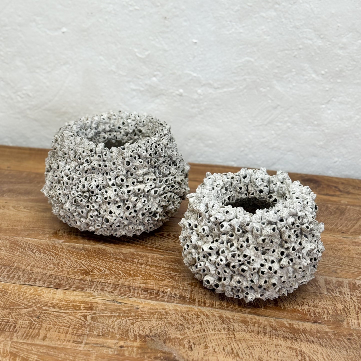 Two textured ceramic holders on a wooden surface with a white textured wall background