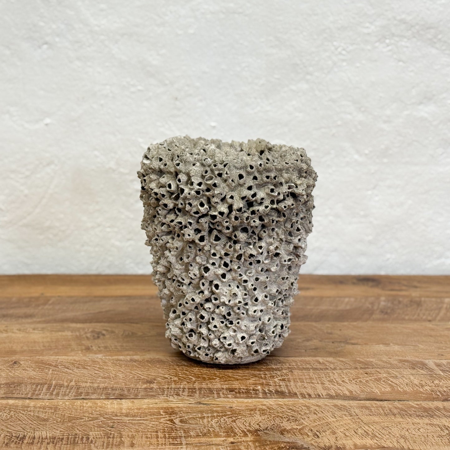 Textured ceramic pot on a wooden surface with a white textured wall background