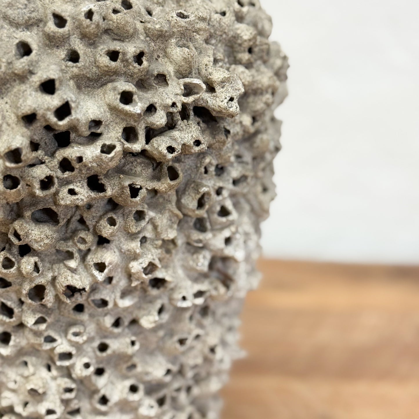 Close-up of a textured ceramic vase on a wooden surface with a blurred background
