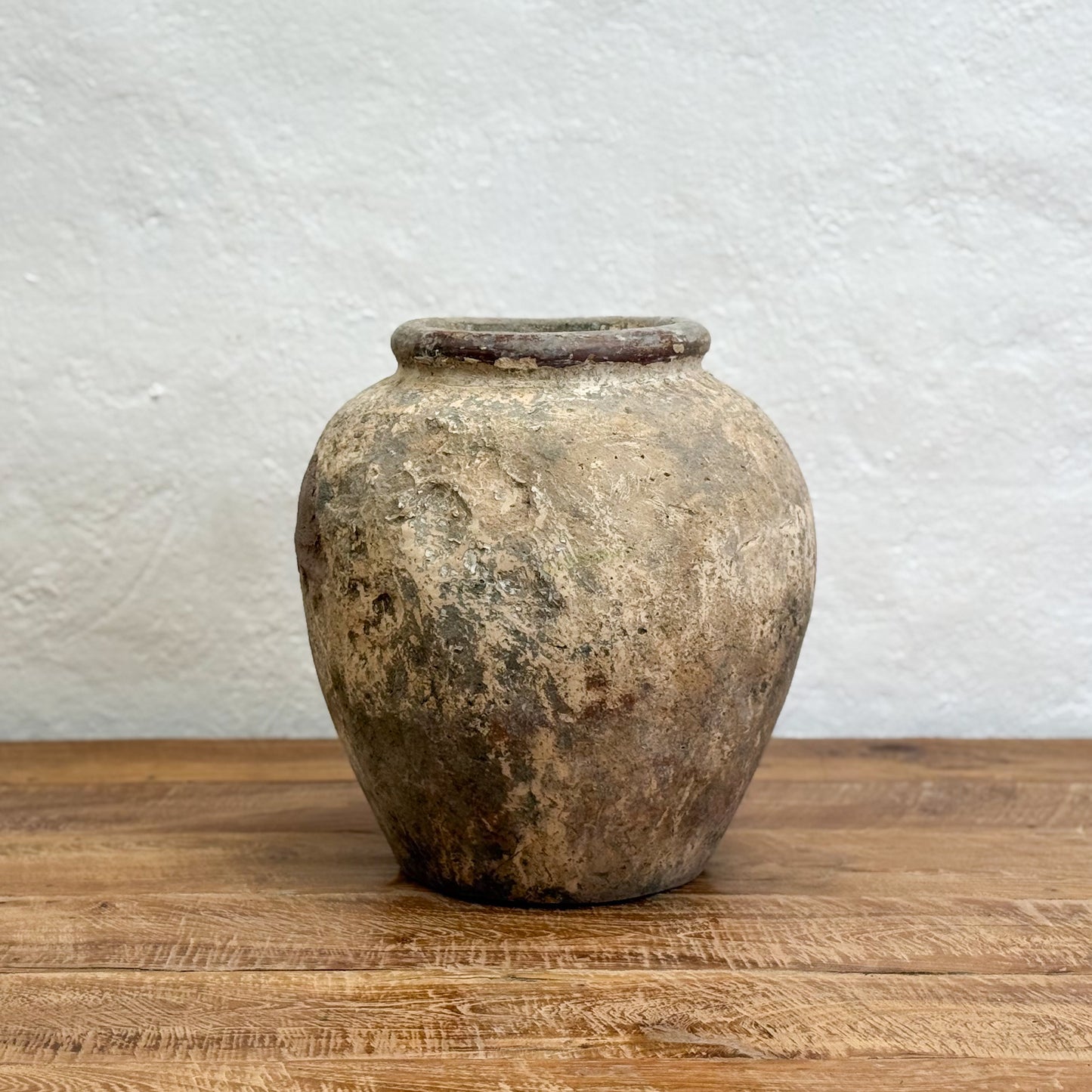 Vintage terracotta jar on a wooden surface with a textured white wall background