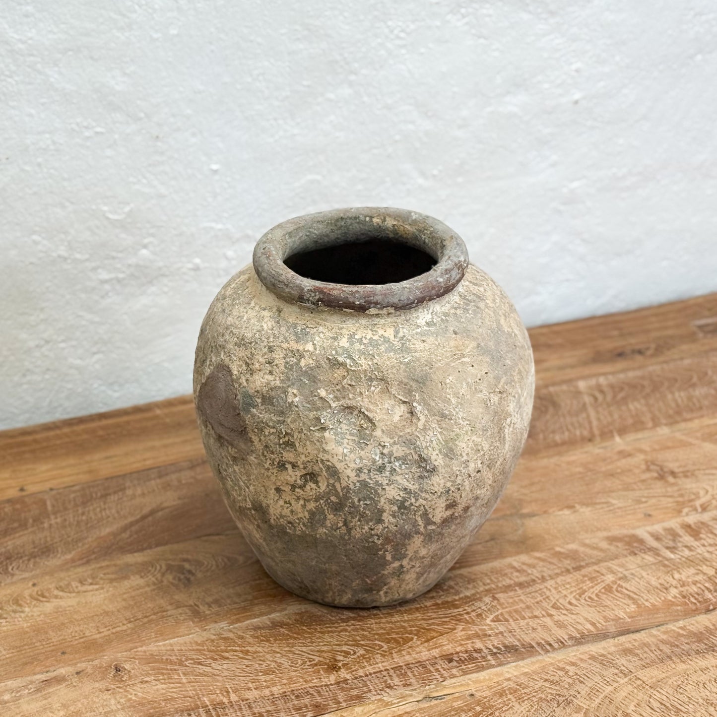 Vintage-style terracotta pot on a wooden surface with a white textured wall background