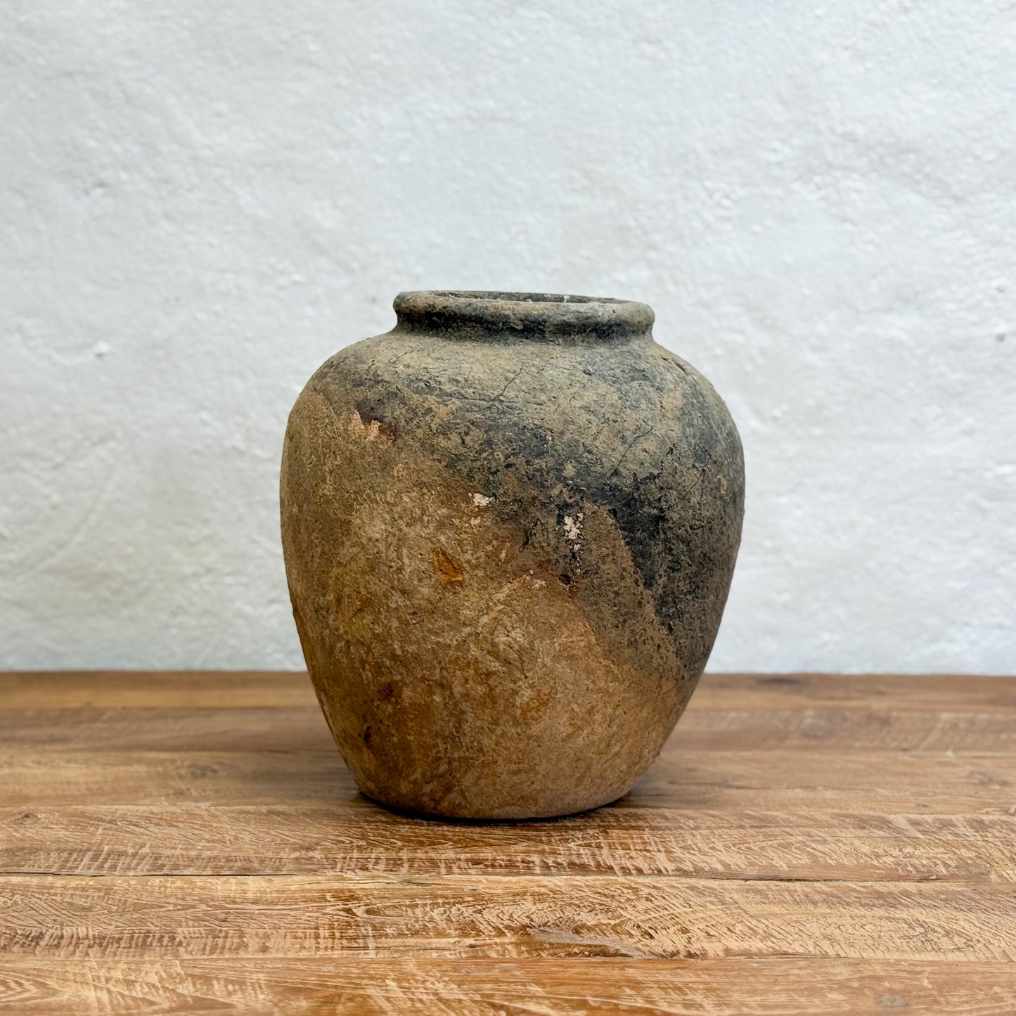 Vintage ceramic jar on a wooden surface with a textured white wall background