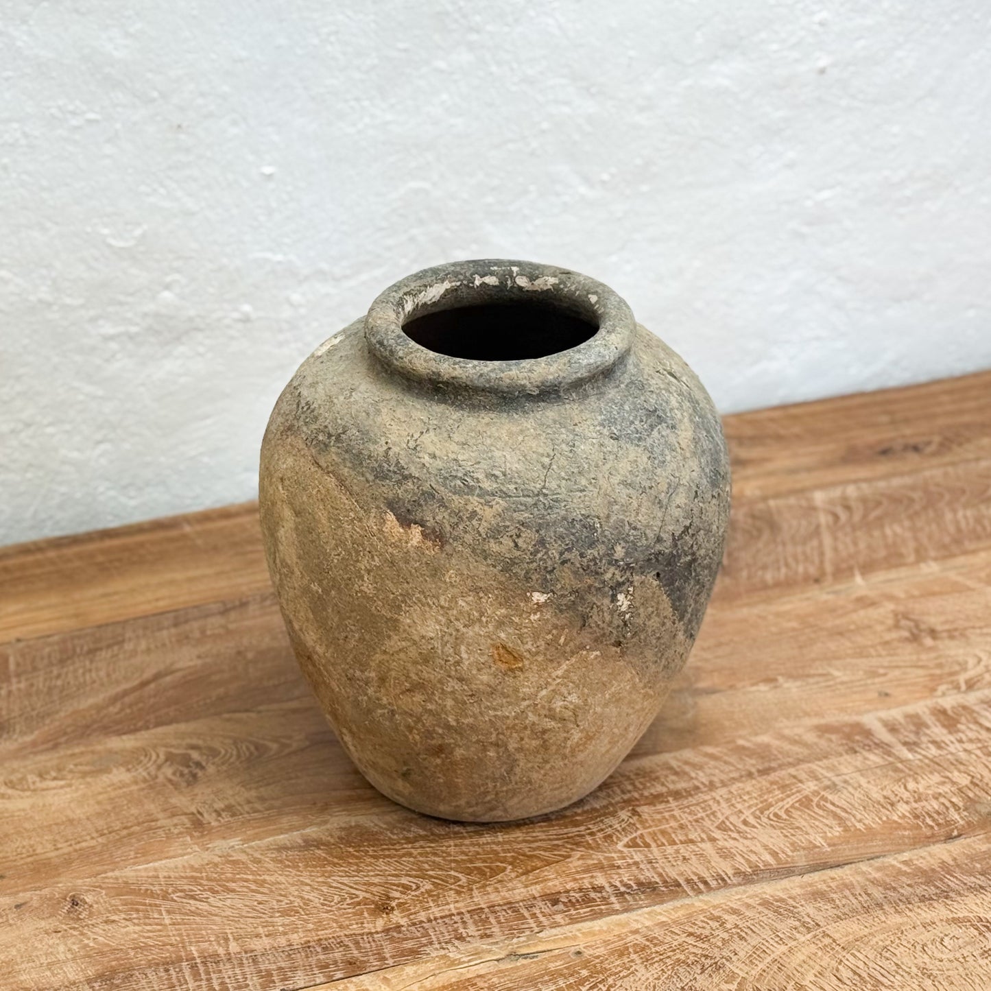 Vintage terracotta pot on a wooden surface with a light gray textured wall background