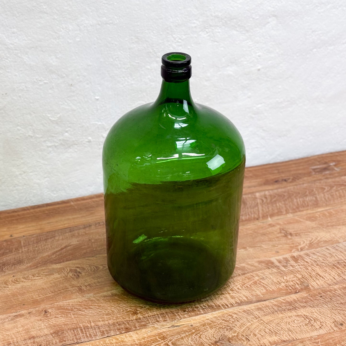 Green glass bottle on a wooden surface with a white wall background