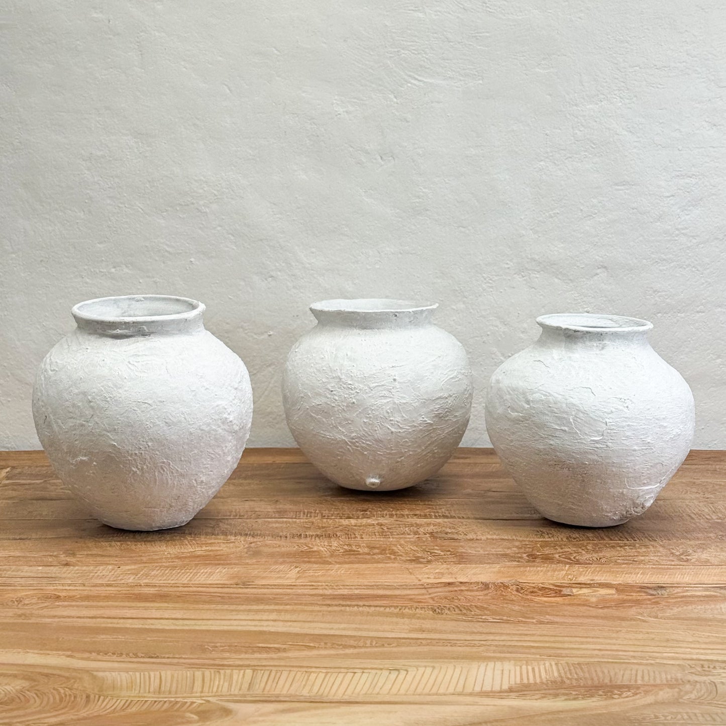 Three textured white vases on a wooden surface with a light gray wall background