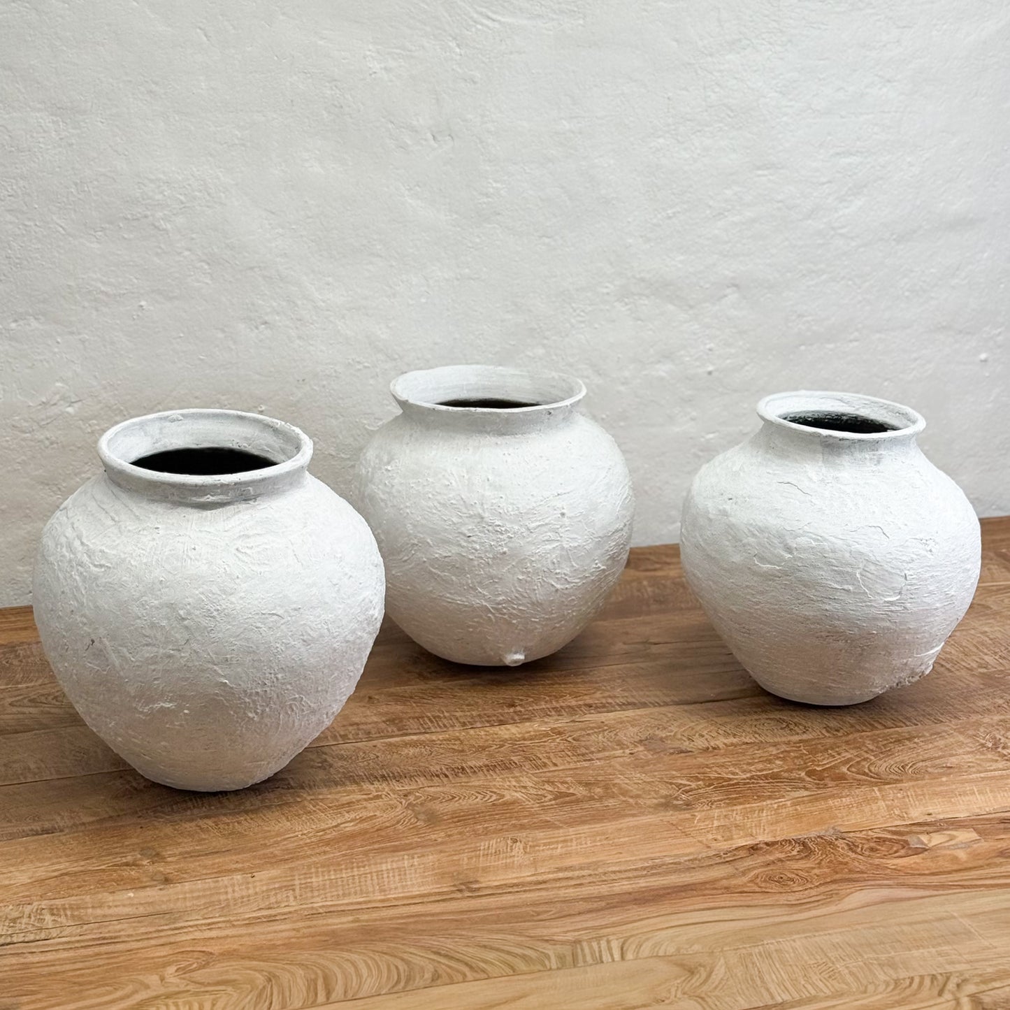 Three white textured vases on a wooden surface with a light gray wall background