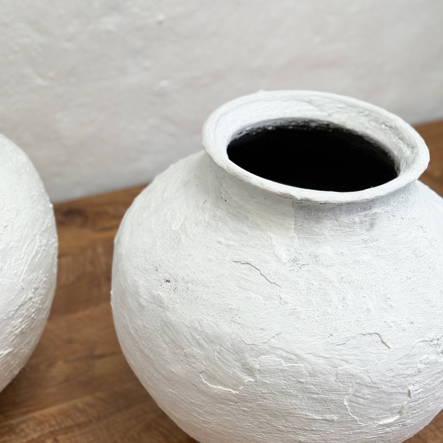Two white ceramic pots on a wooden surface with a neutral background
