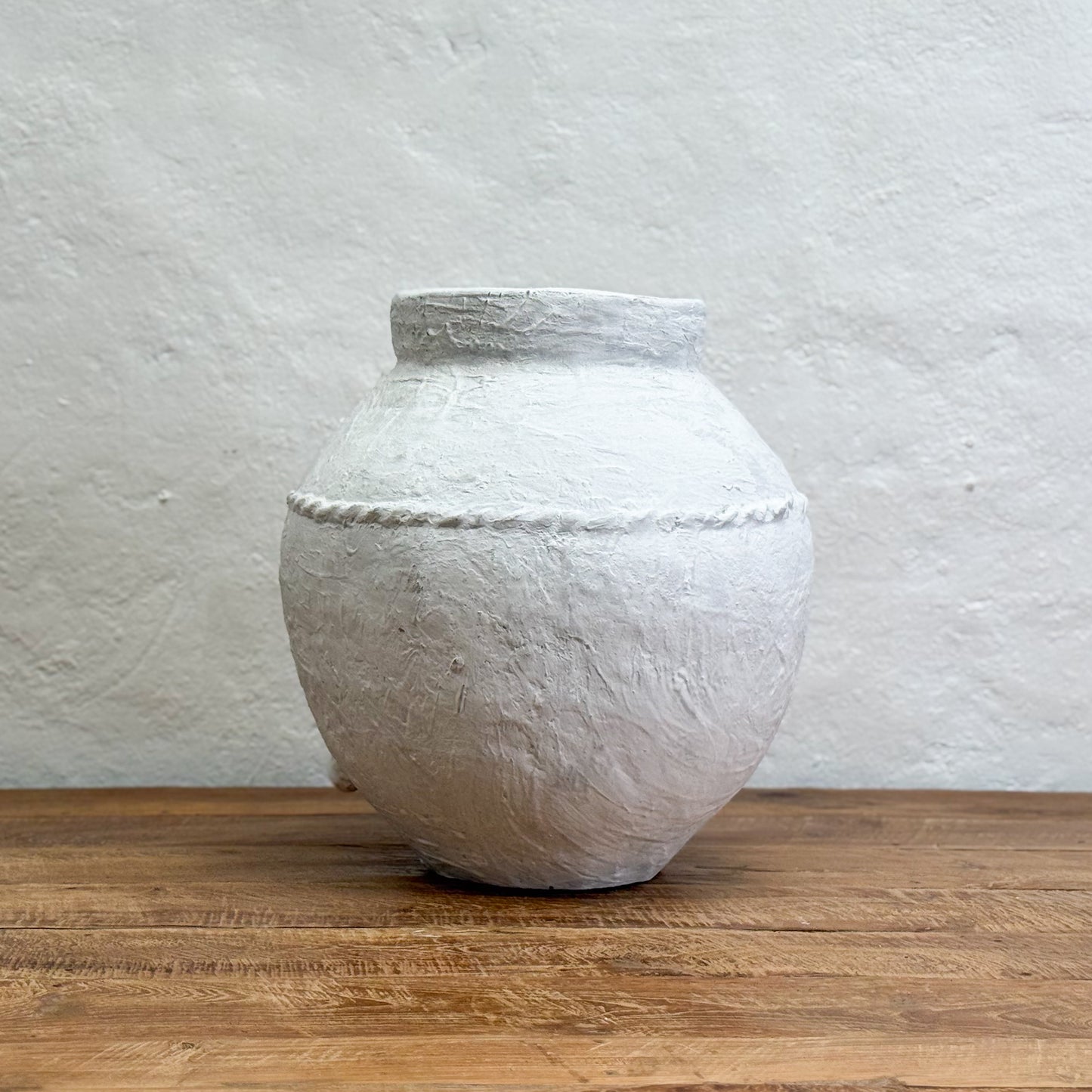 White textured vase on a wooden surface with a light gray background