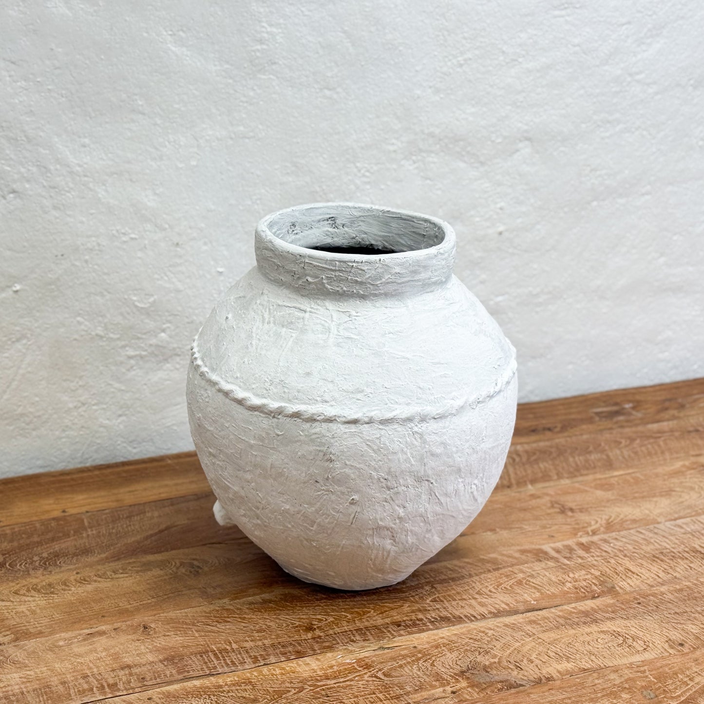 White textured vase on a wooden surface with a light gray wall background