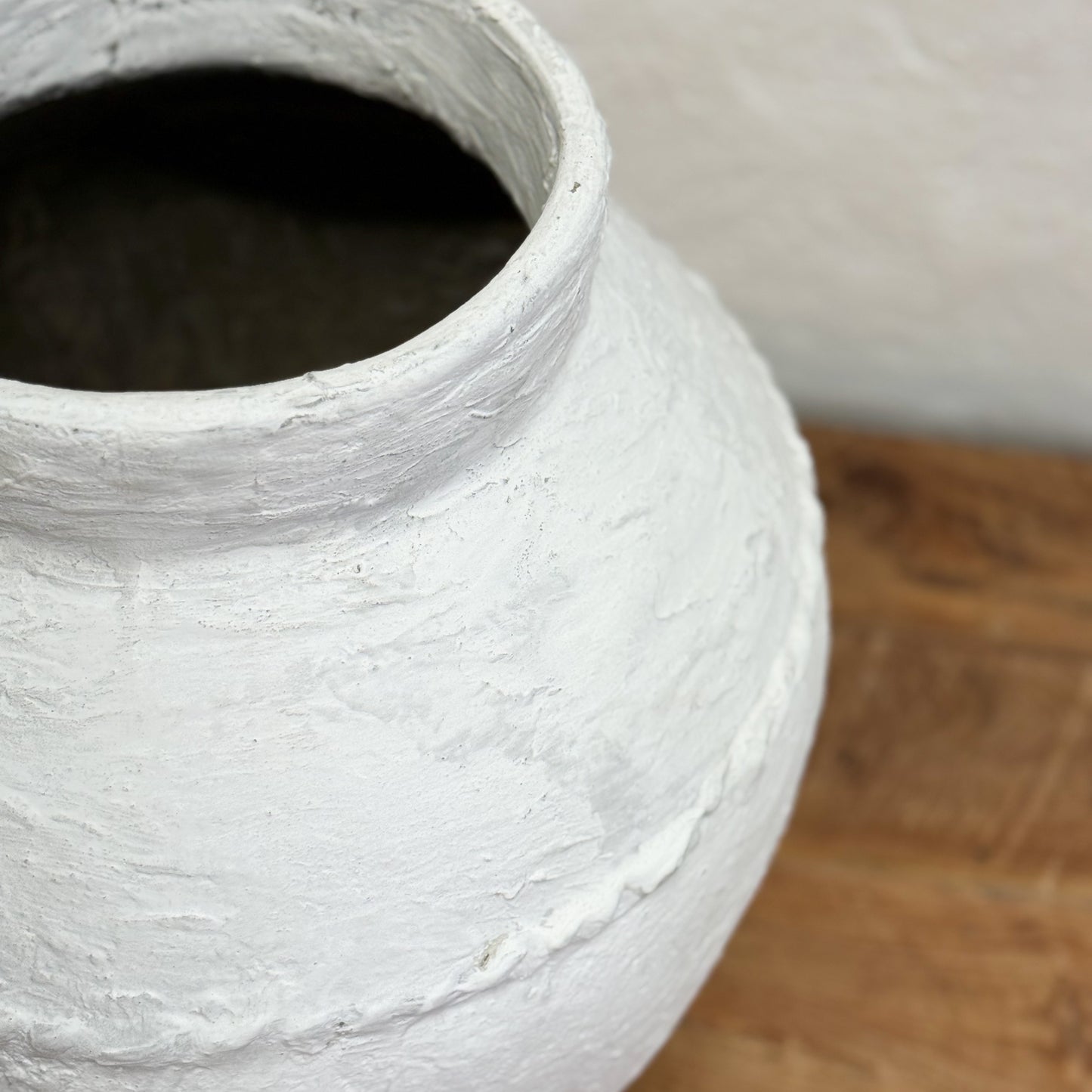 Close-up of a textured white ceramic vase on a wooden surface.