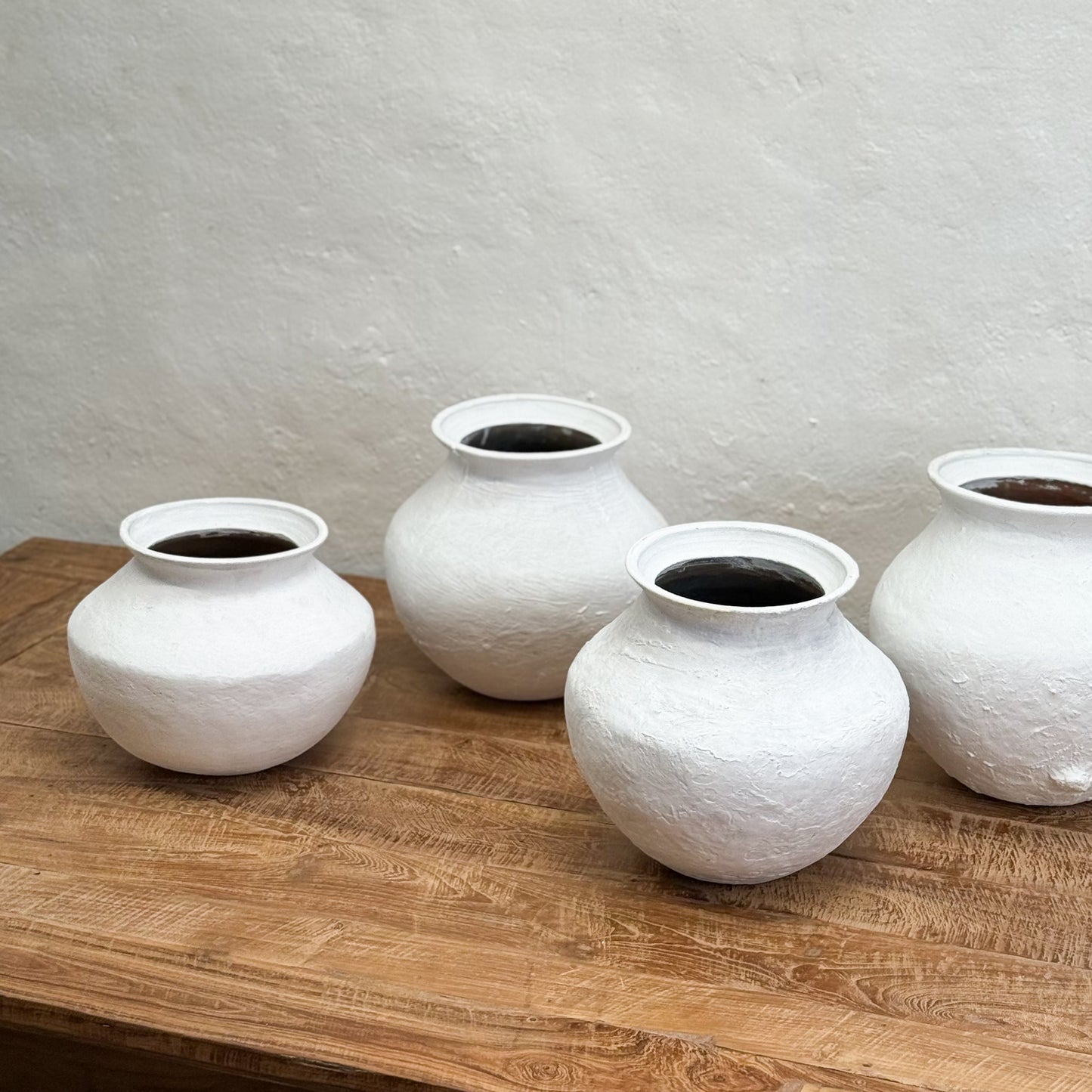 Four white textured vases on a wooden surface with a light gray background