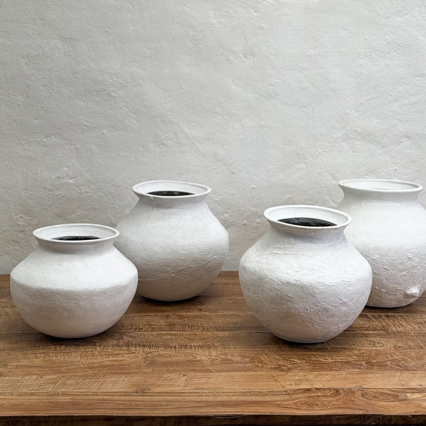 Four white textured vases on a wooden surface with a light gray wall background