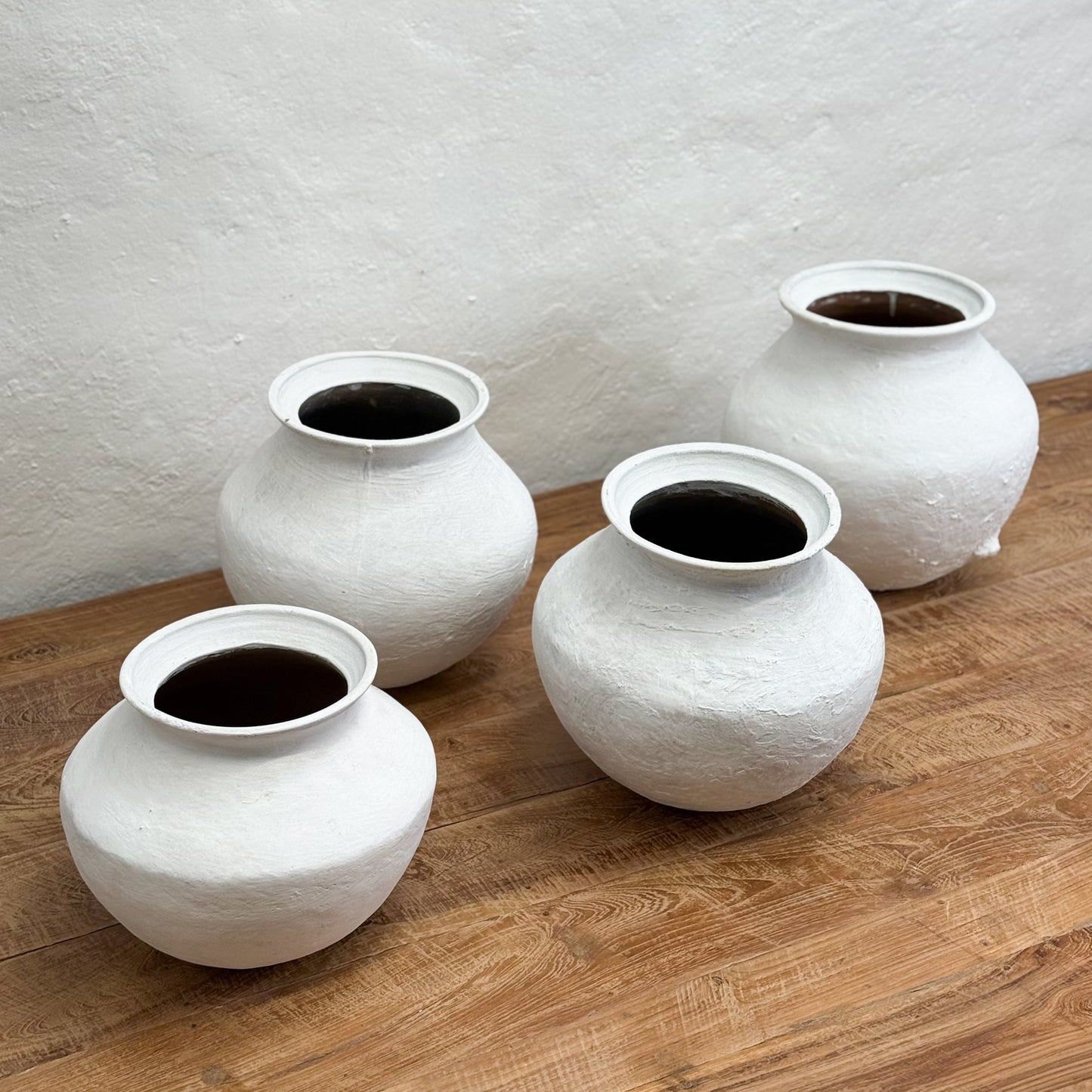 Four white ceramic pots with dark interior on a wooden surface against a light gray wall.