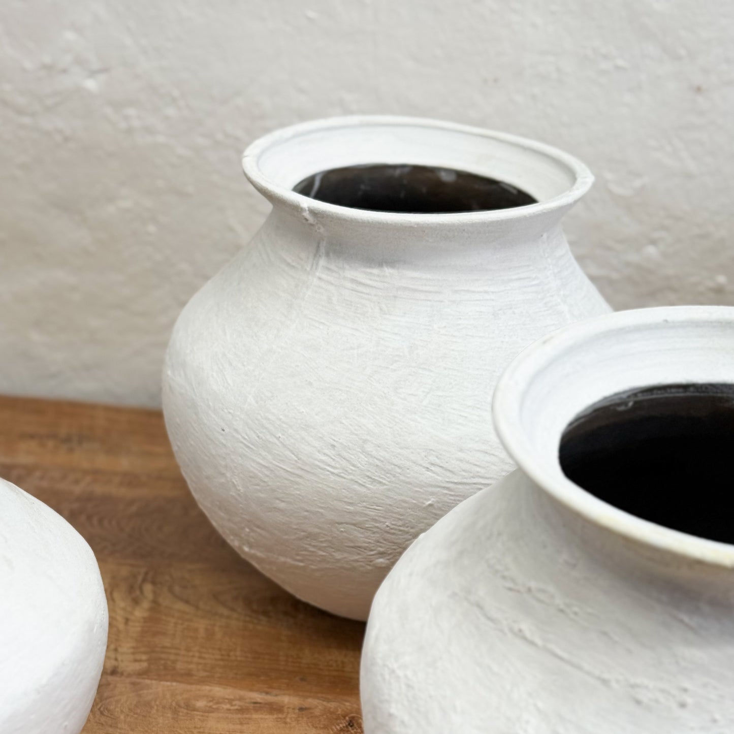 Two white textured vases on a wooden surface with a light gray background