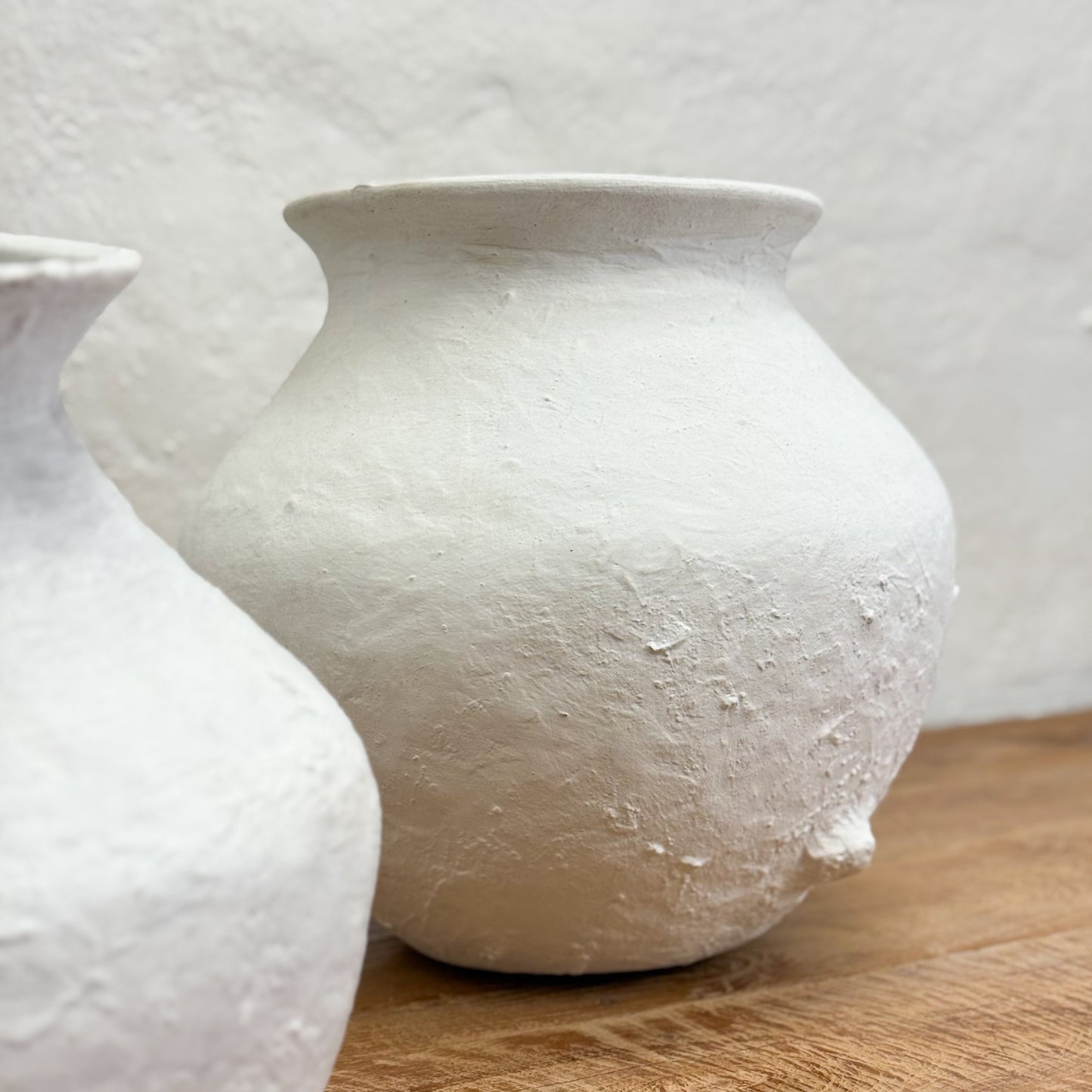 Two white textured vases on a wooden surface with a light background