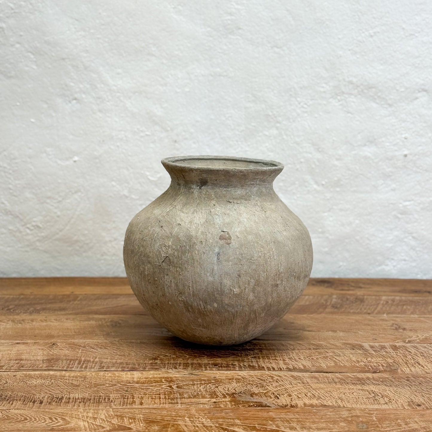 Vintage-style gray ceramic vase on a wooden surface with a textured white wall background
