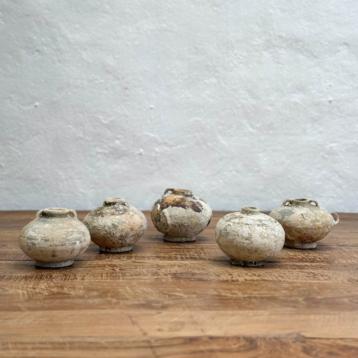 Five rustic ceramic pots on a wooden surface with a gray textured wall background