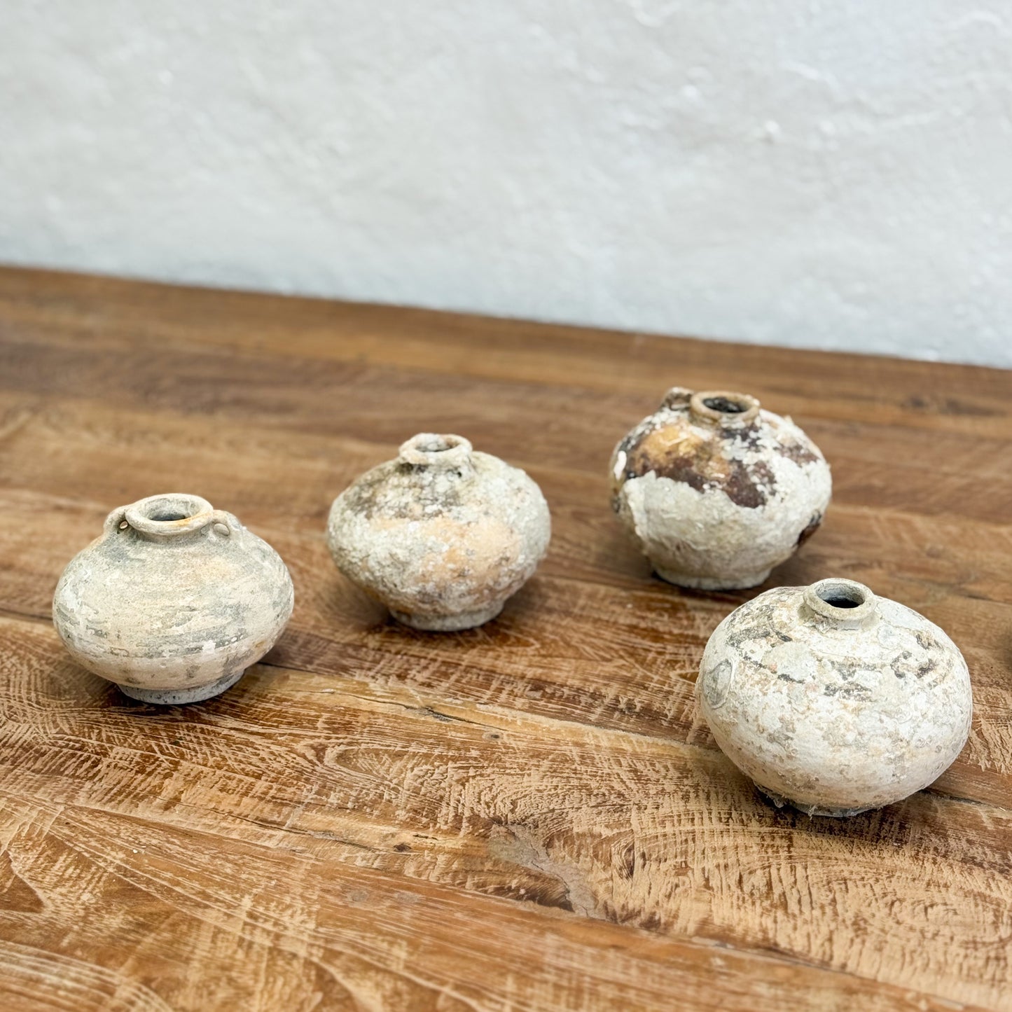 Four small ceramic pots on a wooden surface with a white background