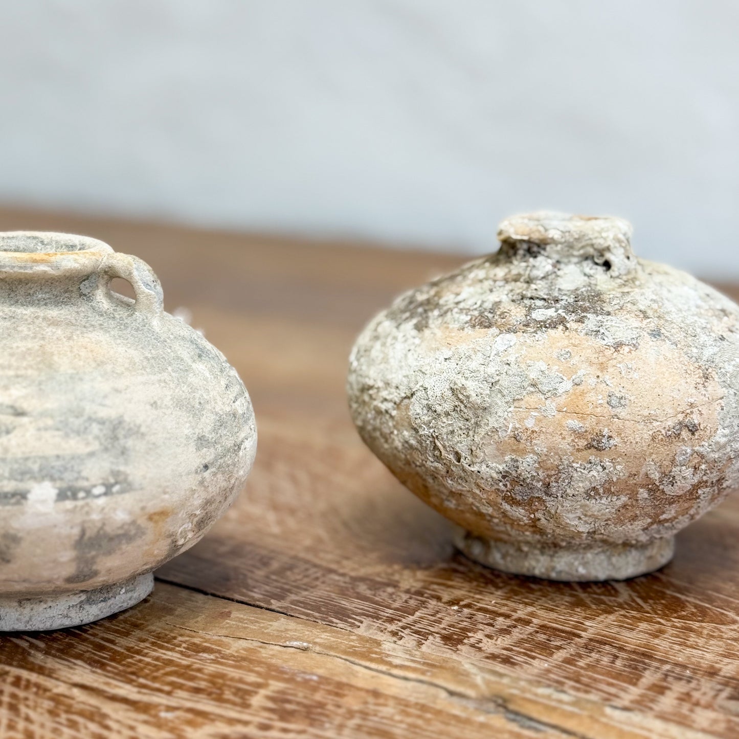 Two ancient clay pots on a wooden surface with a neutral background