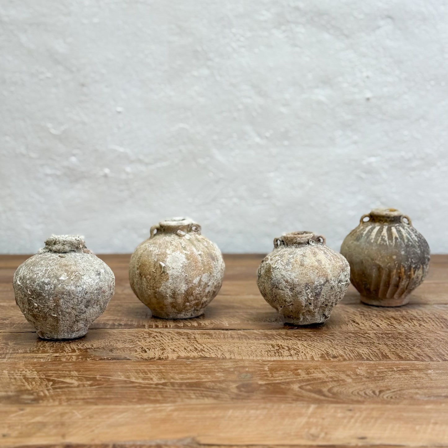 Four rustic ceramic jars on a wooden surface with a textured gray wall background