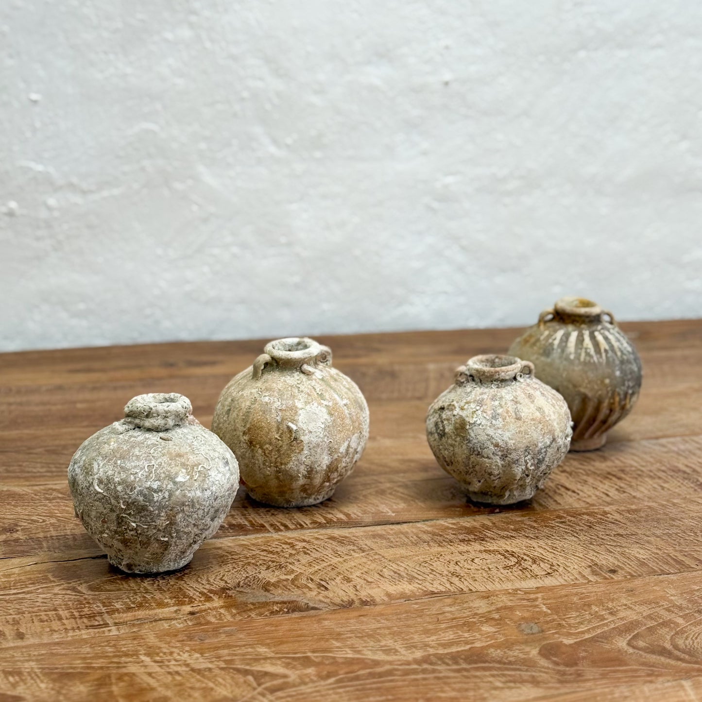 Five rustic clay pots on a wooden surface with a textured white wall background