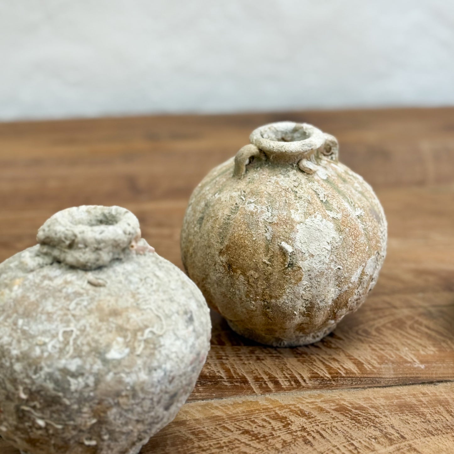 Two rustic clay pots on a wooden surface with a neutral background