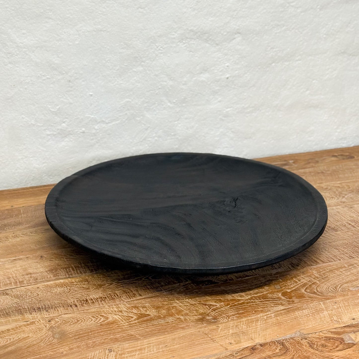 Black round stone plate on a wooden surface with a white textured wall background