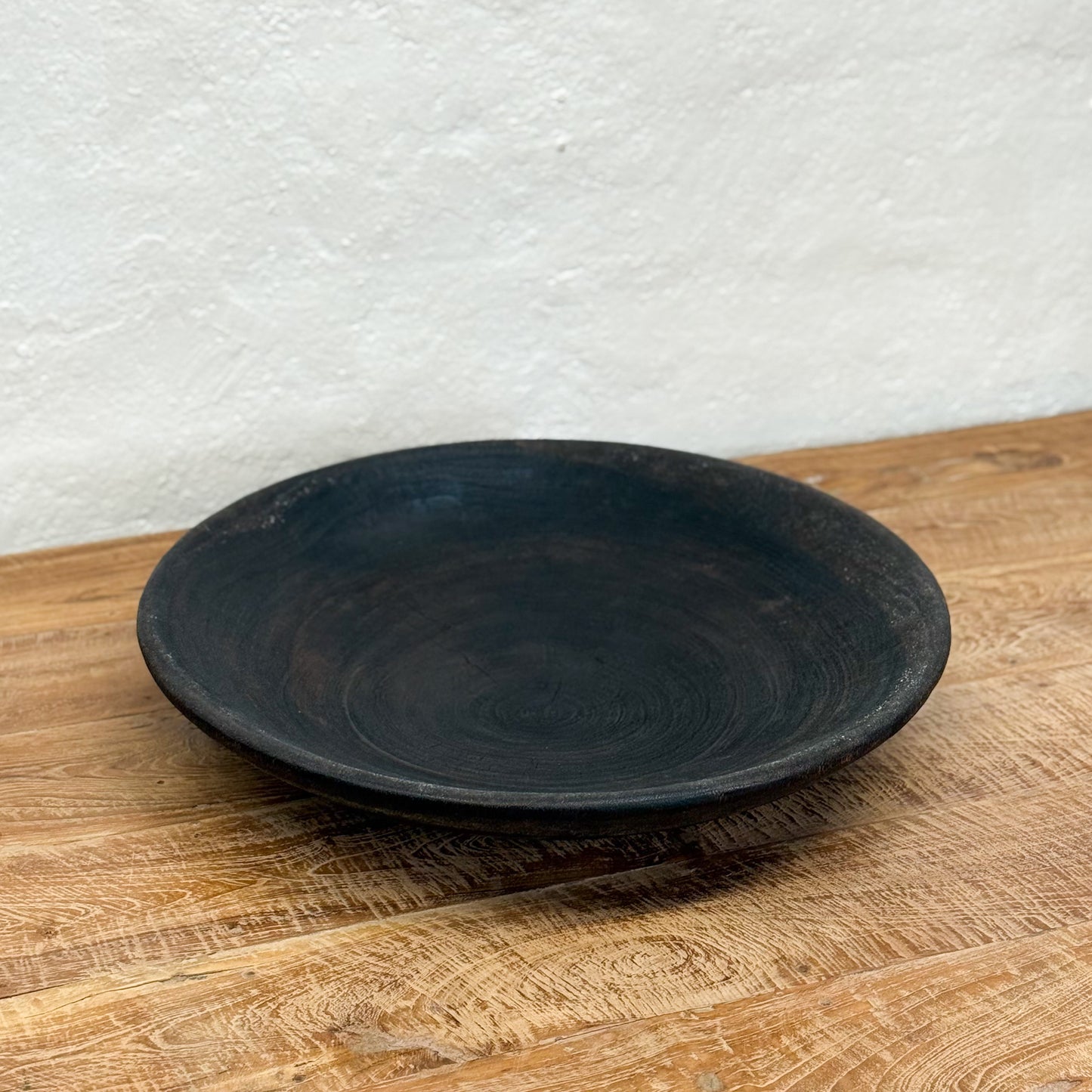 Black ceramic plate on a wooden surface with a white textured wall background