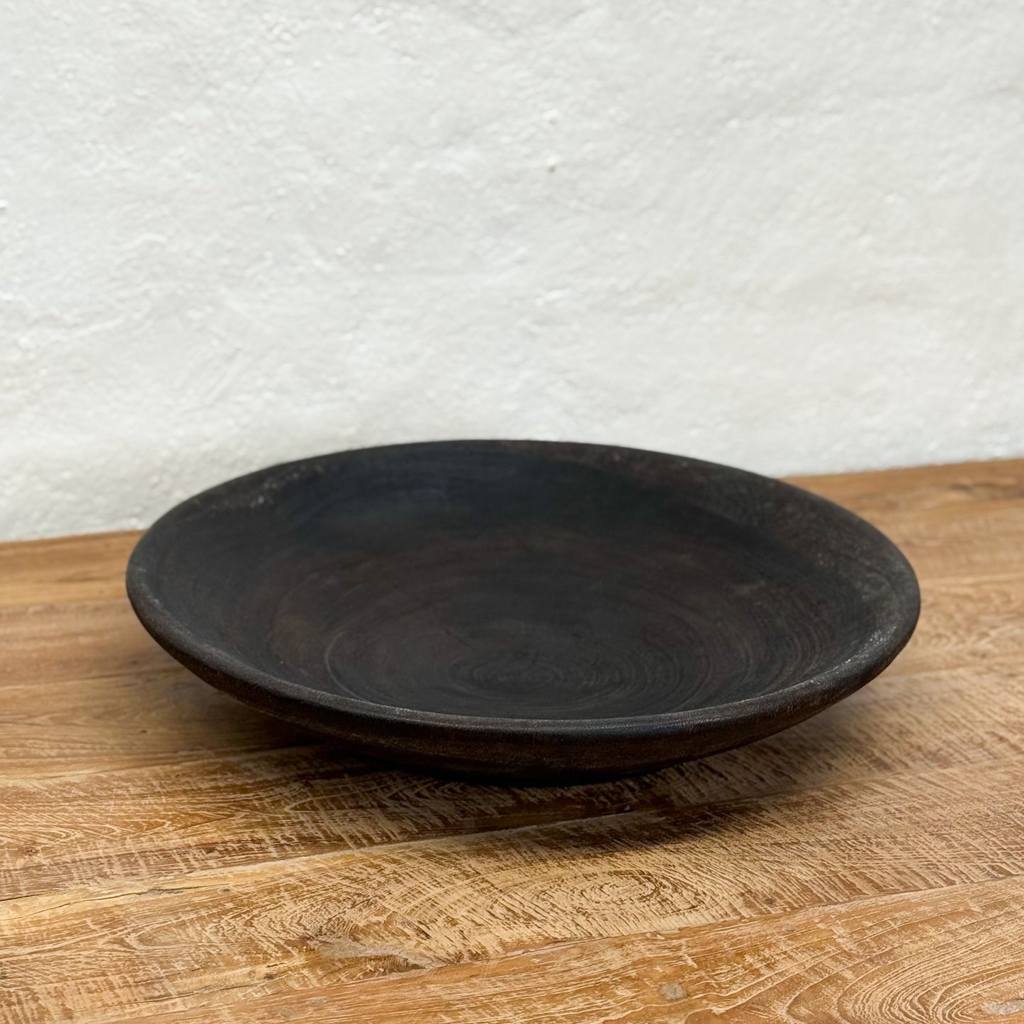 Black ceramic plate on a wooden surface with a white textured wall background