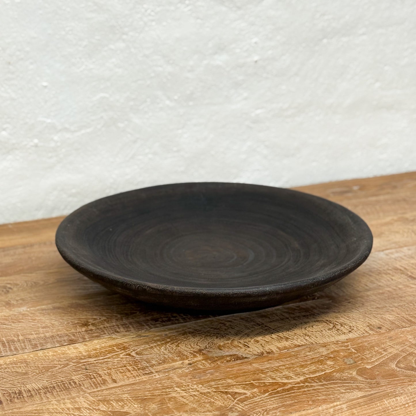 Black ceramic plate on a wooden surface with a white textured wall background