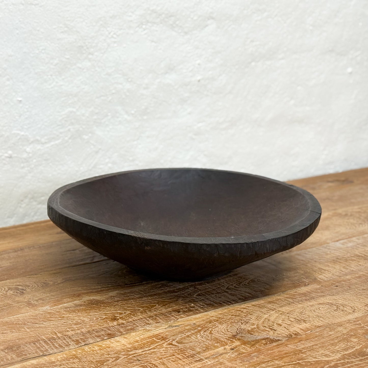 Black wooden bowl on a wooden surface with a white textured wall background
