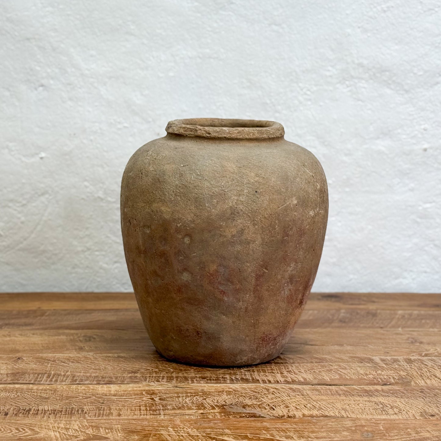Vintage terracotta jar on a wooden surface with a white textured wall background