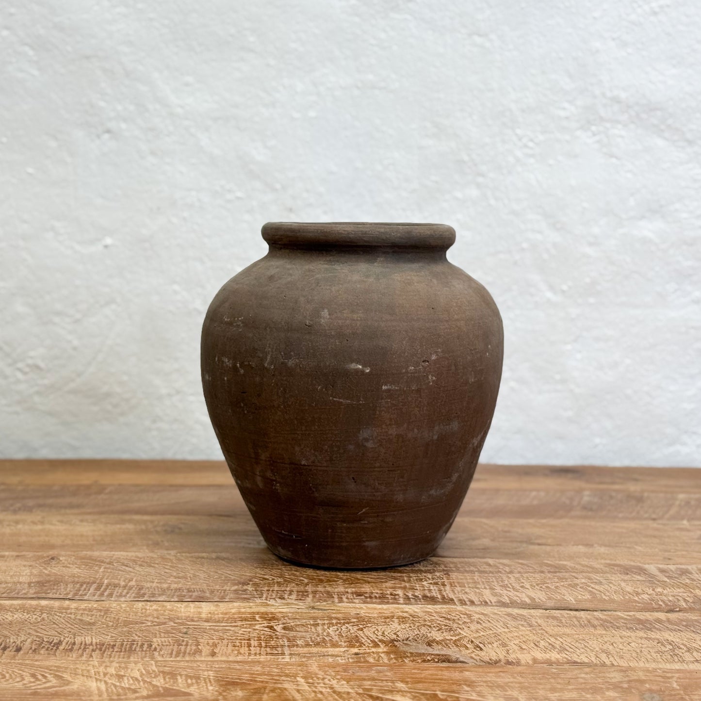 Brown clay pot on a wooden surface with a light gray textured background