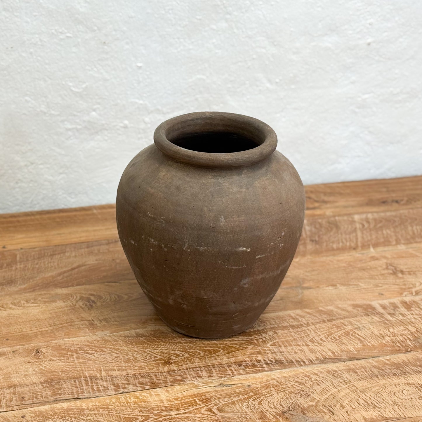 Brown clay pot on a wooden surface with a white textured wall background