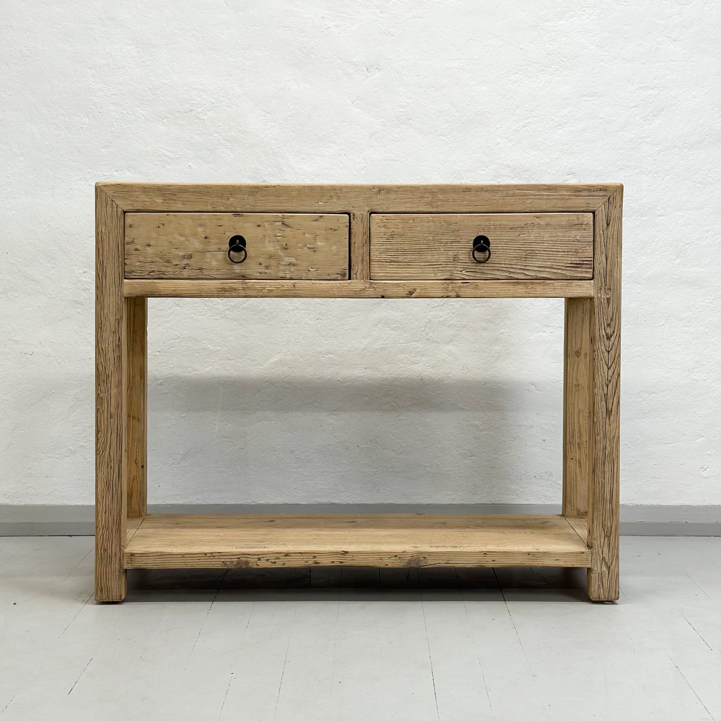 A brown elm wood console table with two drawers and a lower shelf, placed against a plain wall on a white floor.